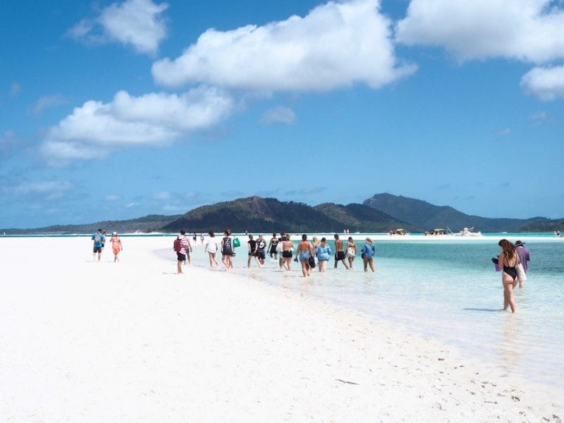 Barrera de Coral fotografía de un grupo de jóvenes de espalda que anda por la playa de las islas Whitsundays. Al fondo las montañas